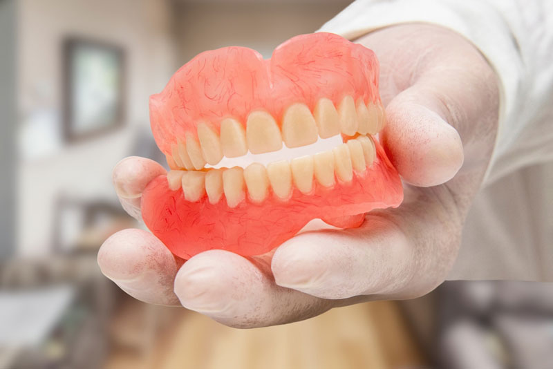 Dentist holding full upper and lower dentures in a clinical setting at Grace Dental in Framingham, MA